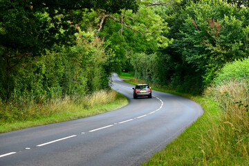 Moving car on a winding road in the woods in summer, West Midlands, England, UK