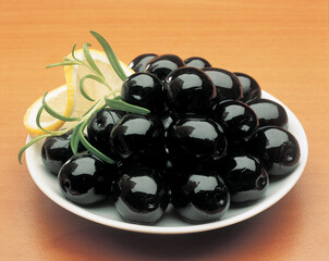 Olives in a white bowl on a wooden table, top view