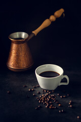 Black coffee in a white cup next to spilled coffee beans