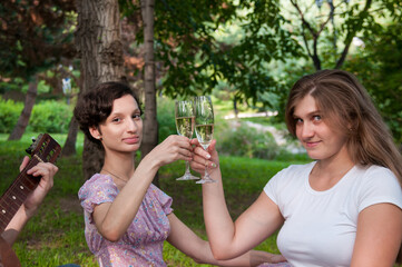 Two girls are sitting with glasses of wine at a picnic in the summer in the park