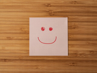 A paper sticker pasted on a wooden surface with the image of the happy smiley character