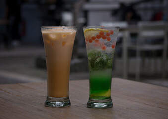 a glass of iced Thai tea and a mojito on a wooden table
