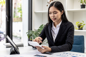 Businesswoman using a white calculator, a financial businessman examining the numerical data on a company financial document, she uses a calculator to verify the accuracy of numbers.