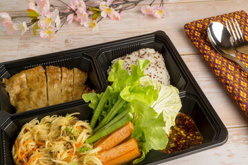 A Box Set of Vegetarian Spicy Papaya Salad, Vegetarian Grilled Chicken, Quinoa Sticky Rice and Fresh Vegetables, served on wooden table