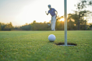 Golfer action to win after long putting golf ball on the green golf, lens flare on sun set evening time.