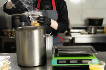 Food delivery. In the restaurant, the chef prepares food and prepares it in disposable dishes. closeup female hands pour broth with sausages into lunch boxes.