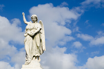Angel statue standing against clouds blue sky.