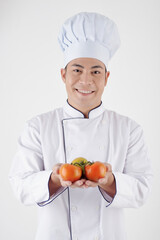 Studio portrait of smiling restaurant chef in uniform holding red tomatoes