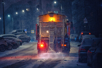 Salt spreading. Snow plow service truck removing snow and spreading salt on snowy city road during...