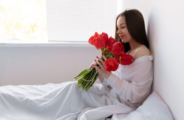 young beautiful woman in the morning in the bedroom sits with a large bouquet of tulips. flowers to a woman for anniversary, valentine's day, or just like that.