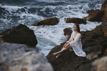 pretty woman with wet hair in a white dress sits on a cliff nature unaltered