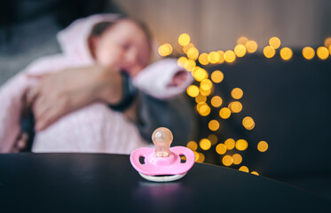 Pink baby pacifier on a blurred background with bokeh lights.