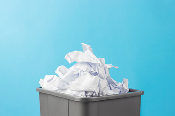 gray trash can full of crumpled paper on a blue background