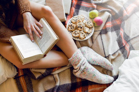 Soft  cozy photo of slim tan  woman in warm sweater  on the bed with  boock  in hands, top view point.  Girl sitting on checkered plaid  near old books.