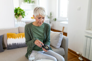 Happy mature woman with glucometer checking blood sugar level at home. Woman testing for high blood...