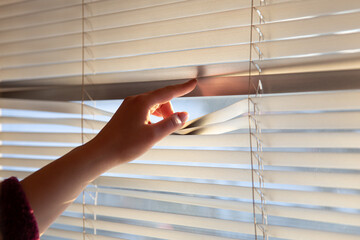 Woman's hand taking a peak through the window blinds.
