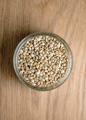 Hemp seeds, edible cannabis production. Marijuana grain in a round glass bowl on wooden texture background.