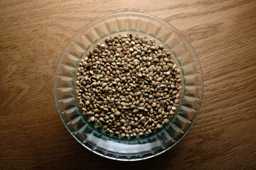 Hemp seeds, marijuana grain in a round glass plate on wooden textured background. Cannabis edible production.