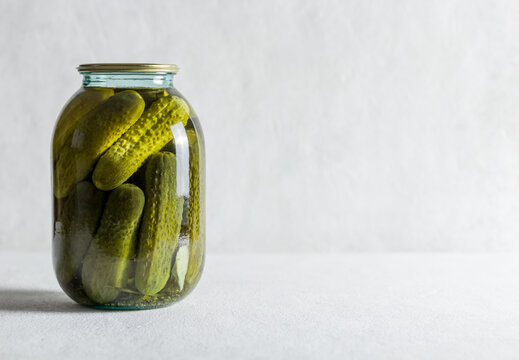 Pickled cucumbers in a glass jar on a light background. Homemade fermented or pickled cucumbers.