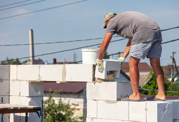 Fototapeta na wymiar A worker builds the walls of a house from aerated concrete bricks.