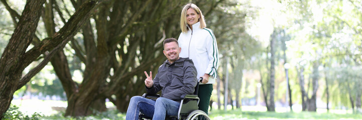 Woman walking in park with disabled man in wheelchair