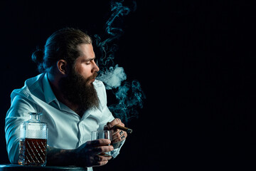 Hipster bearded guy smoke a cigar holds glass of whiskey, blows smoke, dressed in white shirt. 