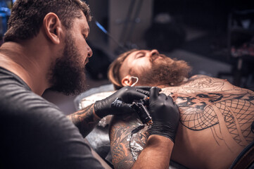 Master of the art of tattooing makes a tattoo on the skin in tattoo parlor
