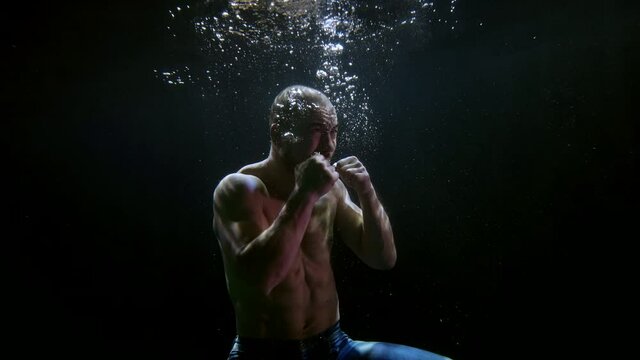 furious agressive man with muscular naked torso is keeping afloat inside water of sea and fighting