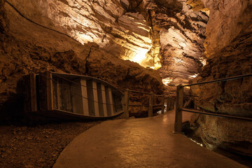 Entrance to an old brown cave illuminated by yellow lights and a small old boat on its side