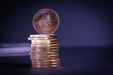 a Krugerrand gold coin stands on a stack of other gold coins