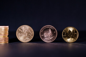 a golden Maple Leaf coin lies next to a Krugerrand coin and a gold dollar