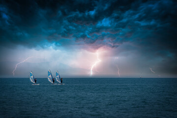three surfers are on the sea and a thunderstorm with lightning rages over the sea