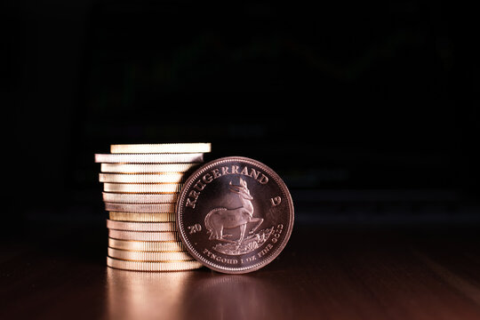 one Krugerrand gold coin stands in front of a stack of gold coins