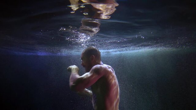 muscular man is fighting alone with invisible enemy underwater, slow motion shot