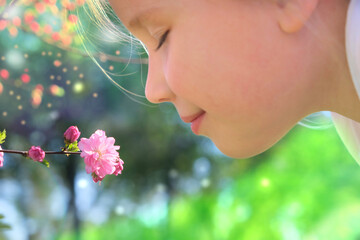 Happy child enjoying nature outdoors. Sunlit  little girl smelling spring blossom  tree. Sakura...