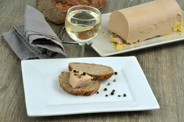 Morceau de foie gras avec des baies et des tartines de pain dans une assiette à côté d'un verre...