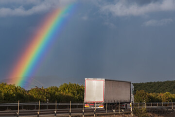 Truck driving on a highway under a rainbow.