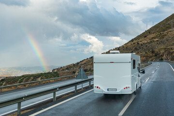 Motorhome driving on the highway on a rainy day and a rainbow in the cloudy sky.