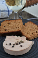 Morceau de foie gras avec des baies et des tranches de pain d'épices dans une assiette à côté d'un verre de vin blanc