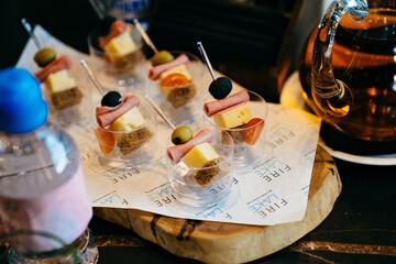 canapes with cheese, ham, tomato and olive on skewers in cups.