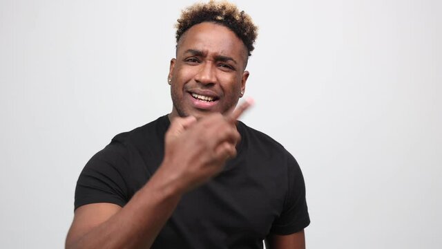 Rude black man with an Afro hairstyle shows his middle finger on an isolated white background. A young African-American man in a black T-shirt looks into the camera and makes a fuck off gesture.