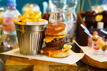 a bucket of fries and mini burger made of bun, cutlet, tomato, cheese and sauce.
