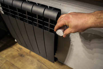 The valve of a home black radiator adjusting the temperature in the room. Hand adjustmen