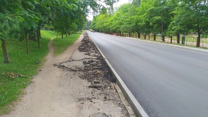 New curbs were installed on the city street and asphalt was laid on the roadway. The next step will be to repair the sidewalk. There is a metal fence on one side of the street, and trees are growing