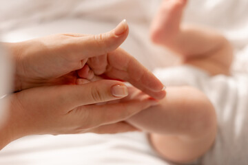 mom kisses the baby's bare feet, holds them in her hands and massages his feet. a child in a white bodysuit on a white bed. healthy active child. High quality photo