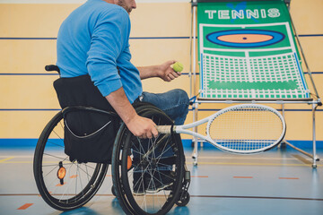 Adult man with a physical disability who uses wheelchair playing tennis on indoor tennis court