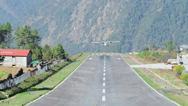 Aeroplane landing on gray runway at mountain small town. Arriving to airfield