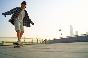 teenage asian boy skateboarding outdoors in city square