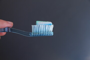 the toothbrush. Blue toothbrush. White and blue toothpaste. Dark grey background.