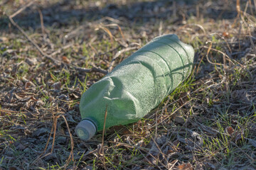 Fototapeta premium Plastic pollution. Plastic bottle covered with hoarfrost lies in the forest. Close-up